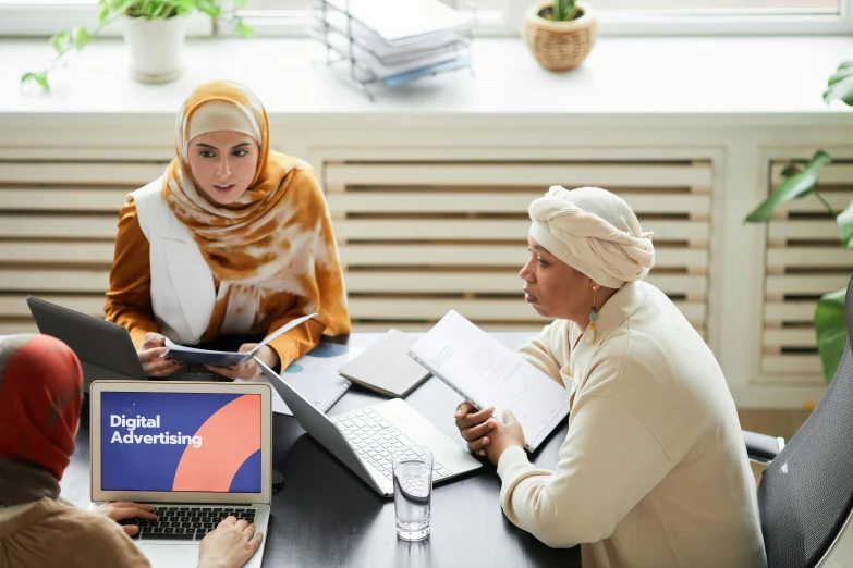 two women with headscarves are sitting at a table with papers