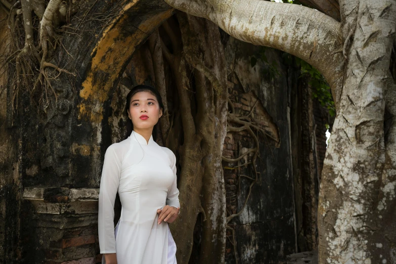 an asian woman standing under some very big trees