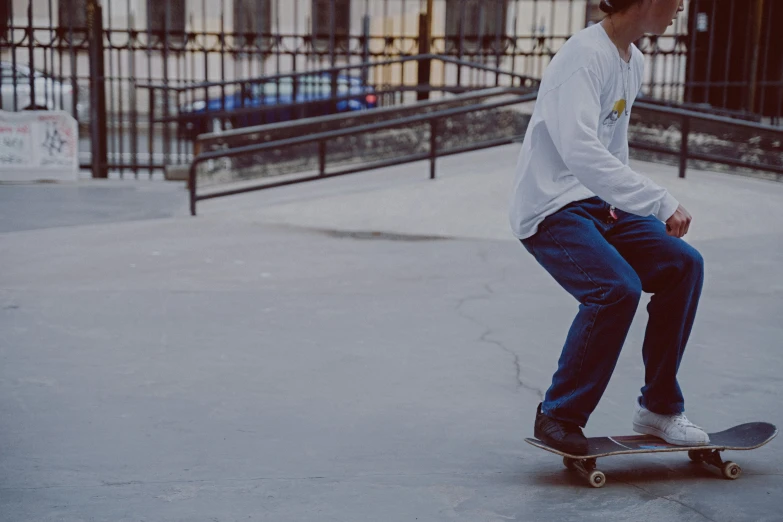 a boy with white shirt on and jeans riding a skateboard