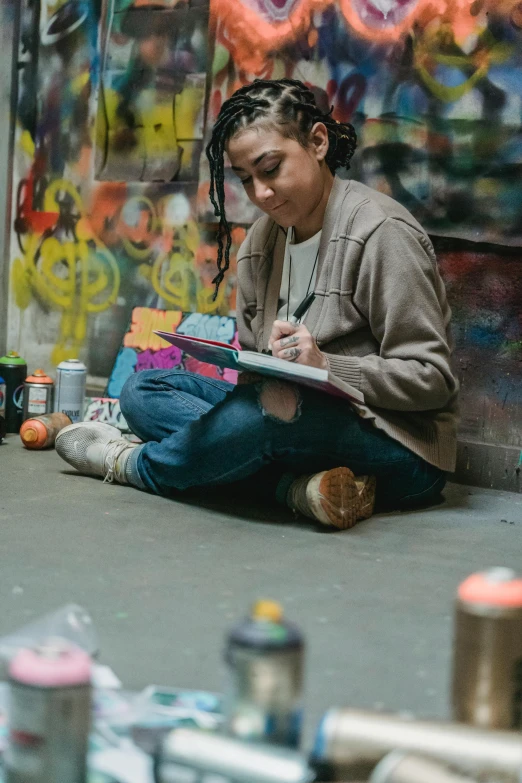 a woman sitting on the floor in front of some graffiti