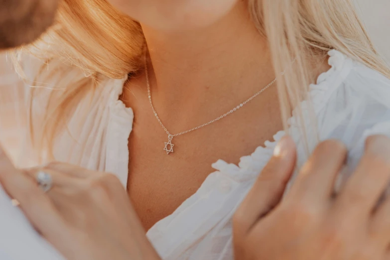 two people, one holding the back of the other with both hands and a diamond necklace