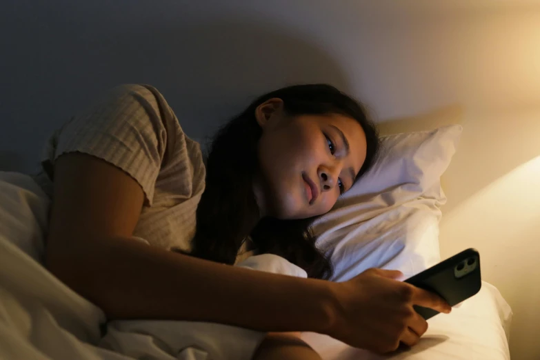 a girl laying in bed with her head down and holding a remote control