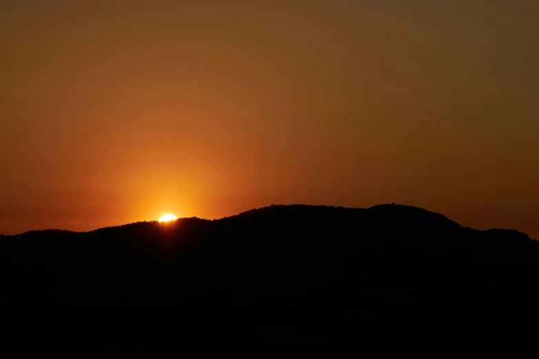 the sun setting behind a mountain with a bird flying over it