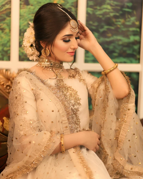 a woman in a white and gold bridal dress, putting on a piece of jewelry