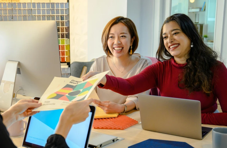 two women with an open laptop computer smiling and showing off their designs