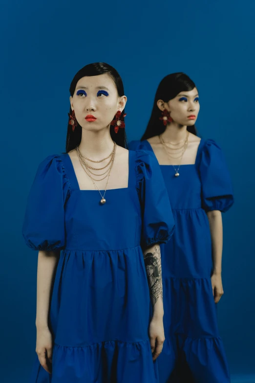 a blue dress with large puffed sleeves on the neck and two girls in similar outfits are standing back to back