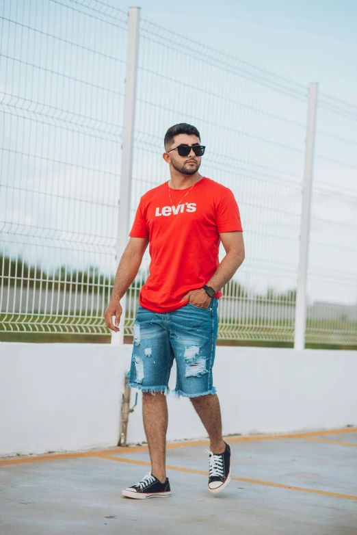 a man in red shirt and jean shorts posing for the camera