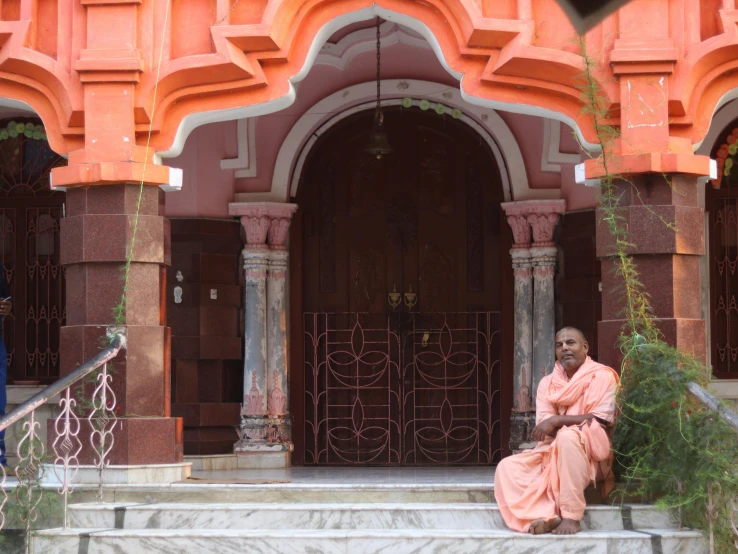 two women dressed in traditional garb sit on steps in front of an ornate doorway