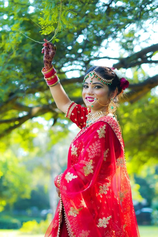 a beautiful woman in a red lehenga holding onto some green leaves