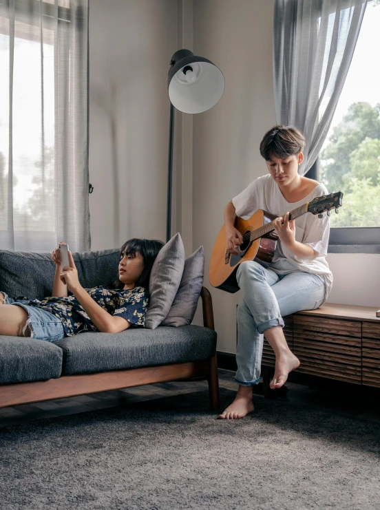 one girl playing the guitar and another woman sitting on a couch