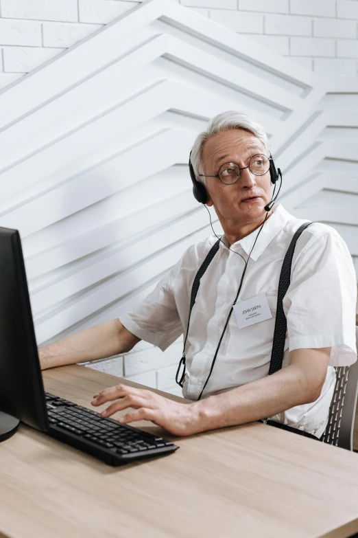 an older man wearing a headset sitting at a computer desk with a keyboard and mouse