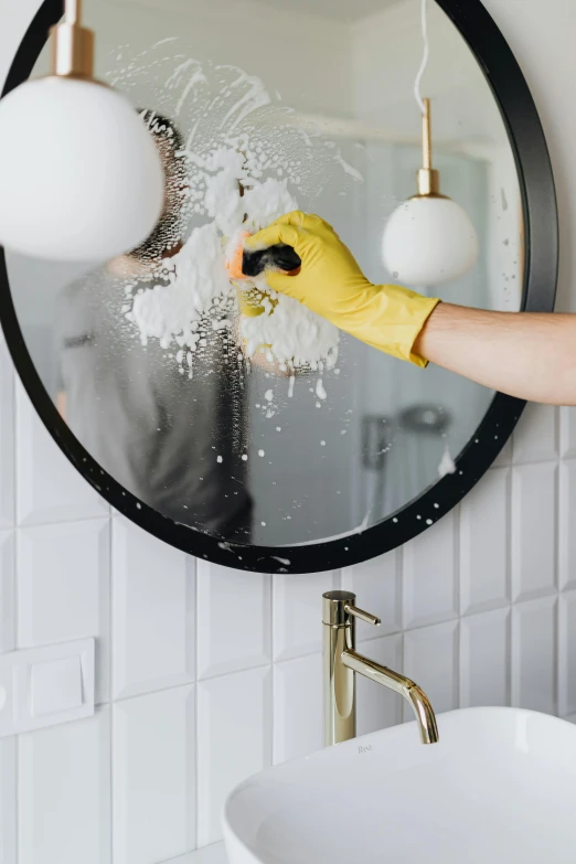 a person in yellow gloves cleaning a mirror