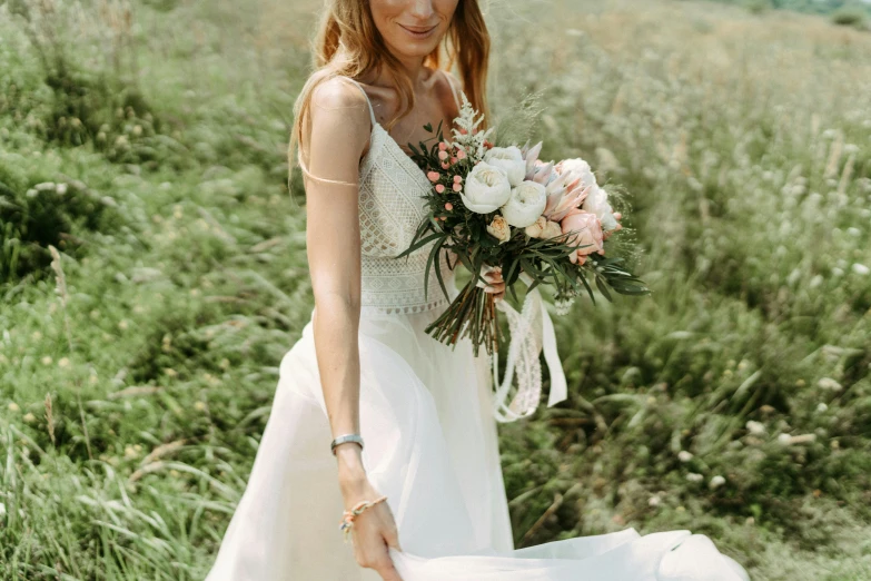 a woman standing in front of a green field holding a bouquet of flowers