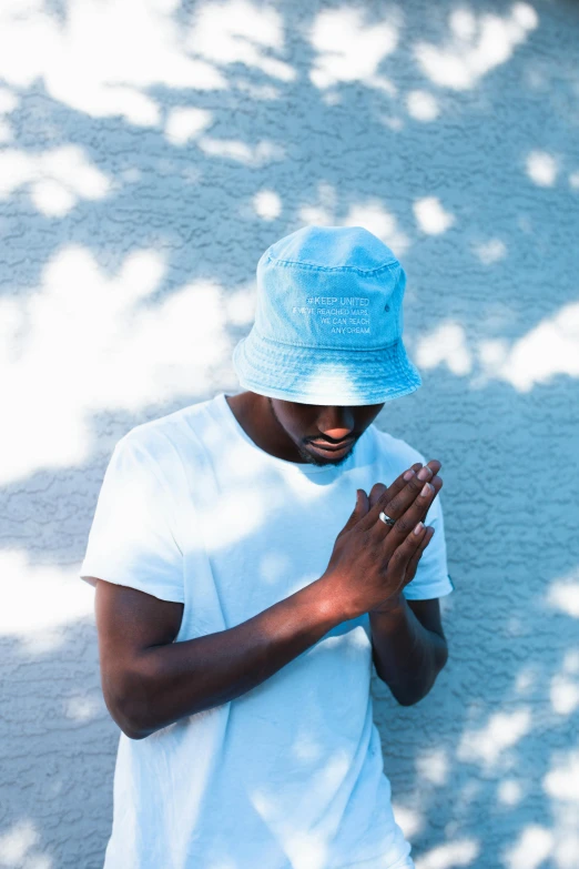 a young black man in a blue cap prays outside