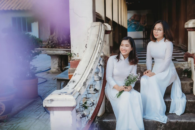 two women in dresses sitting on stairs with flowers