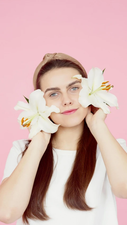 a young woman wearing a white top and holding flowers in her eyes