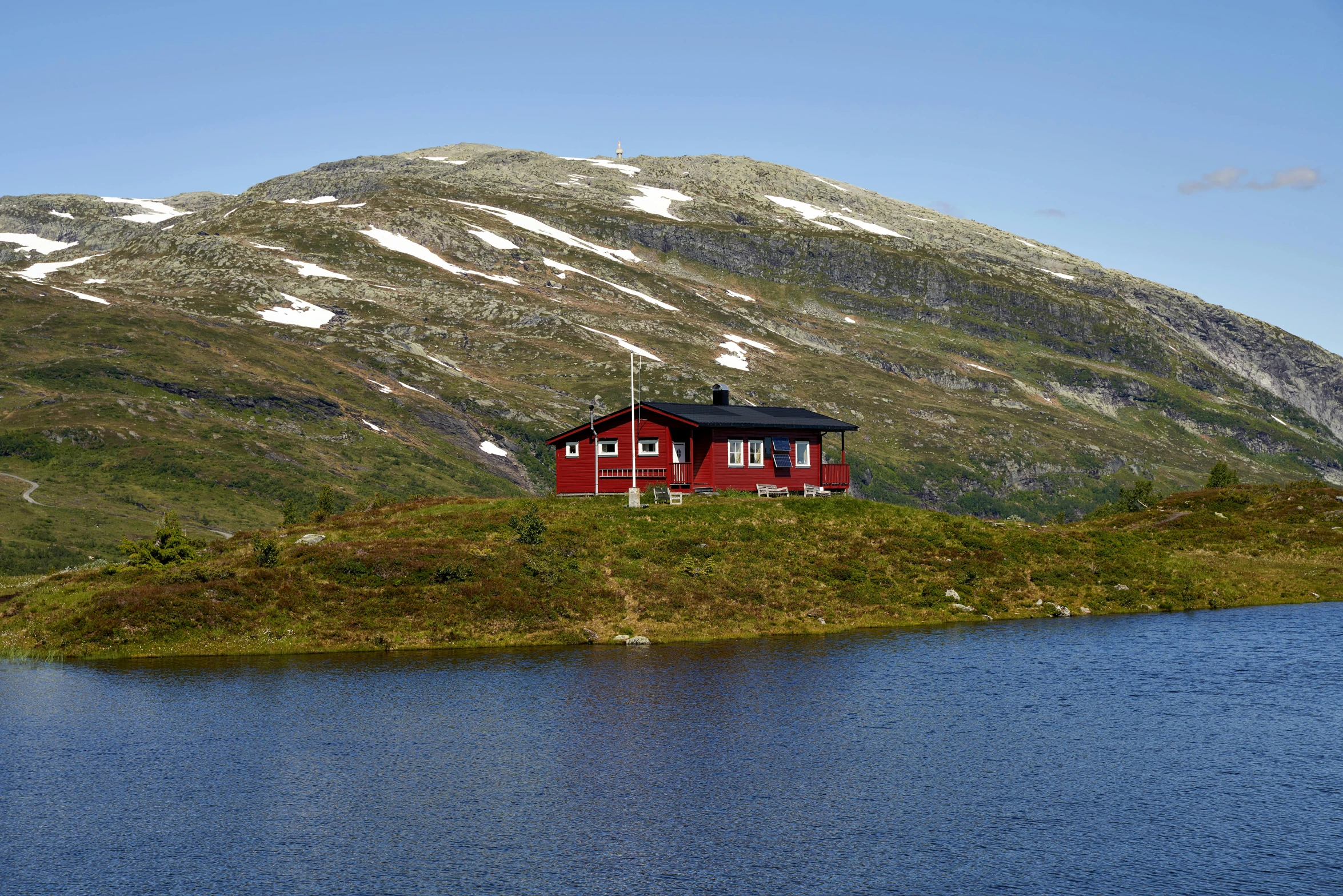 a red house sitting in the mountains next to a lake