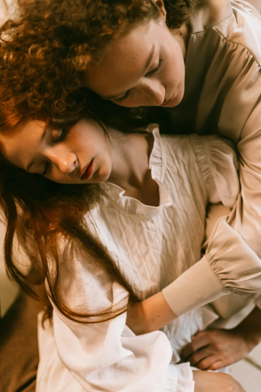 a young woman looking down while her arm around the neck of her younger girl