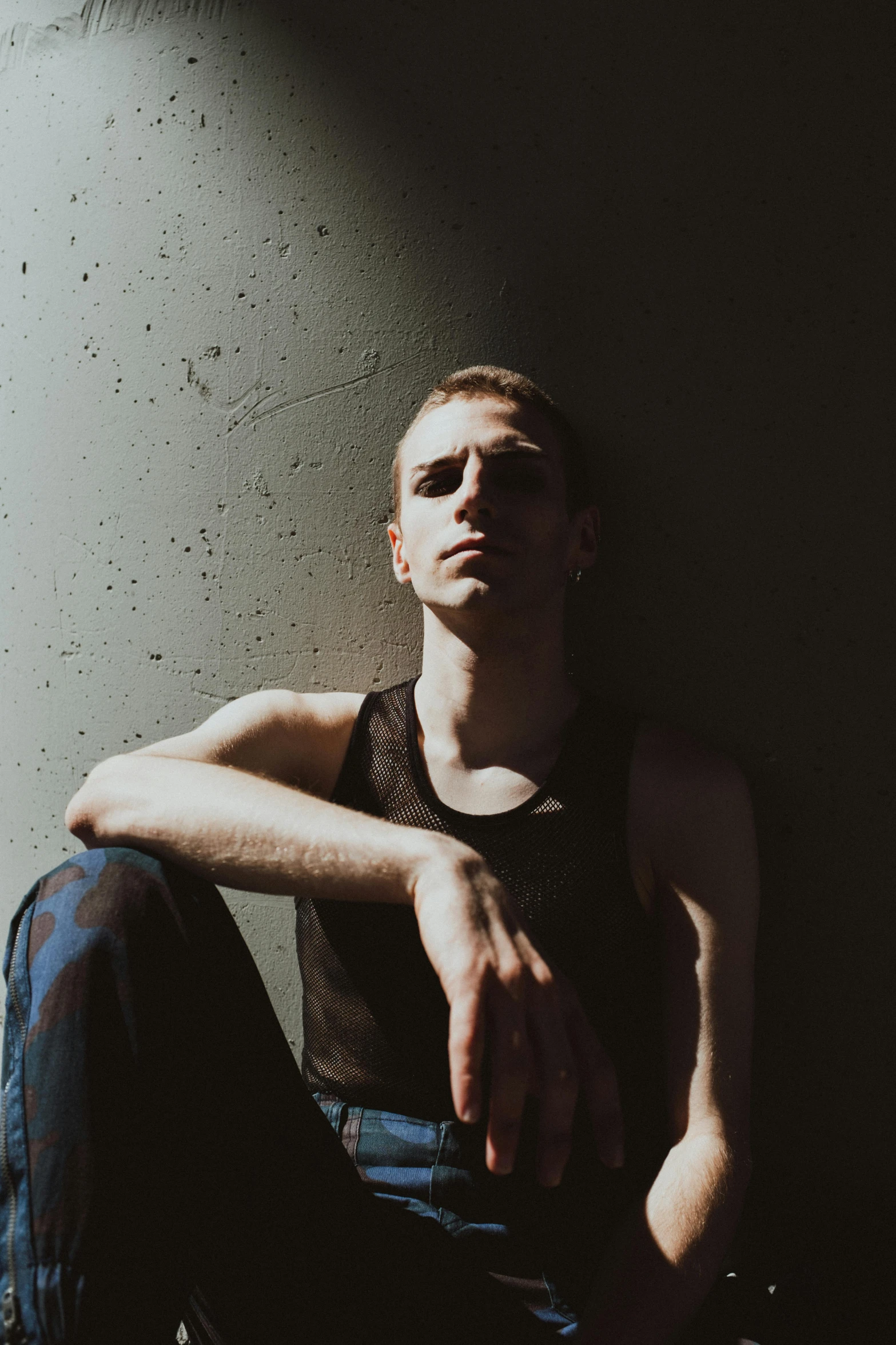 a man sitting against a wall wearing a tank top