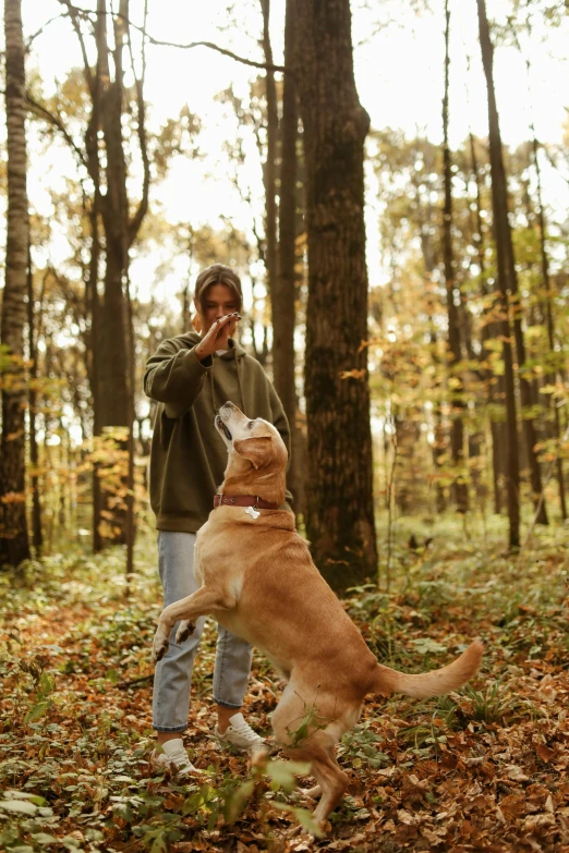 a person talking on a cell phone standing next to a dog in the woods