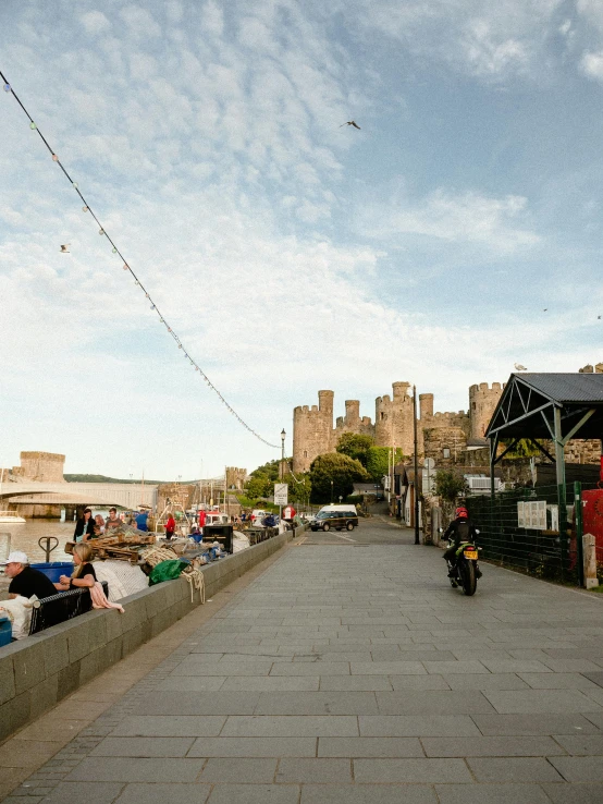 a motorcycle and people walking on a sidewalk near the water