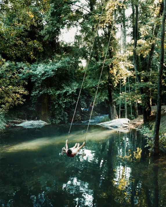 a young woman is swinging off of a rope above a pond