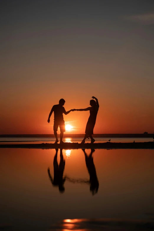 two young men dancing on a beach at sunset