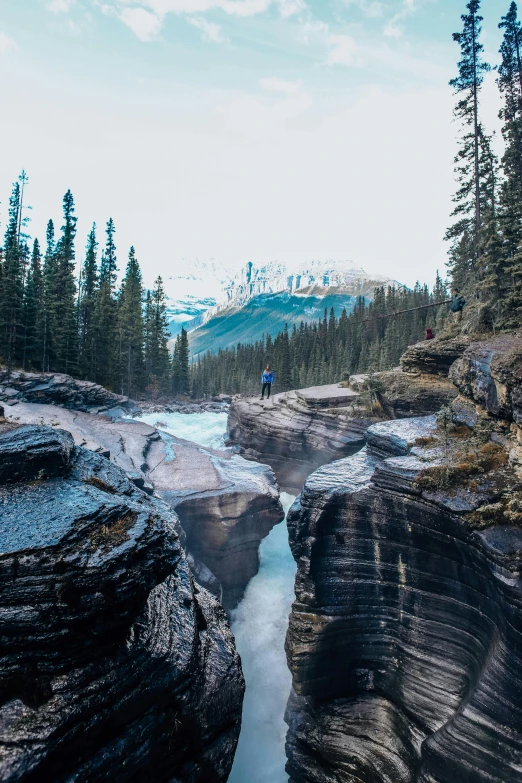 a man is standing on the edge of an outcropping that has a river running through it