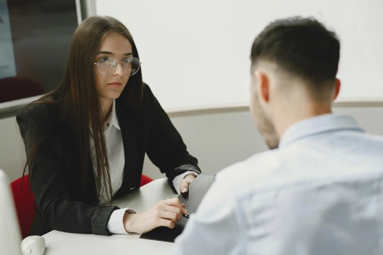 a woman is sitting at a desk in front of a man with glasses