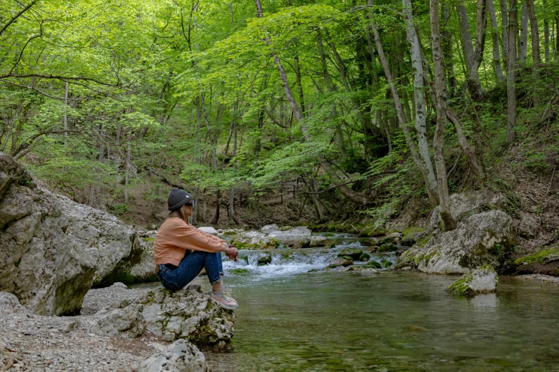 a person sitting on some rocks over looking a stream