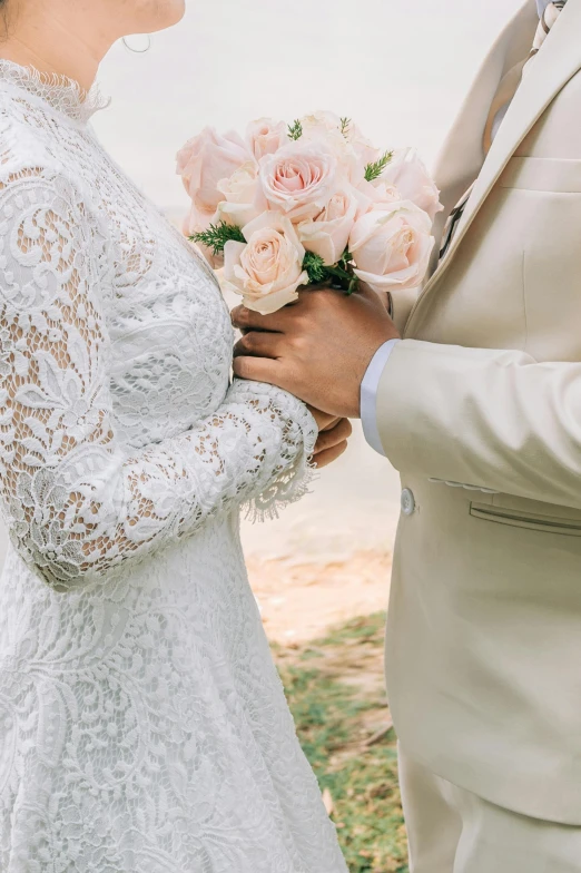 a bride holding a bouquet of roses is holding her groom's hands