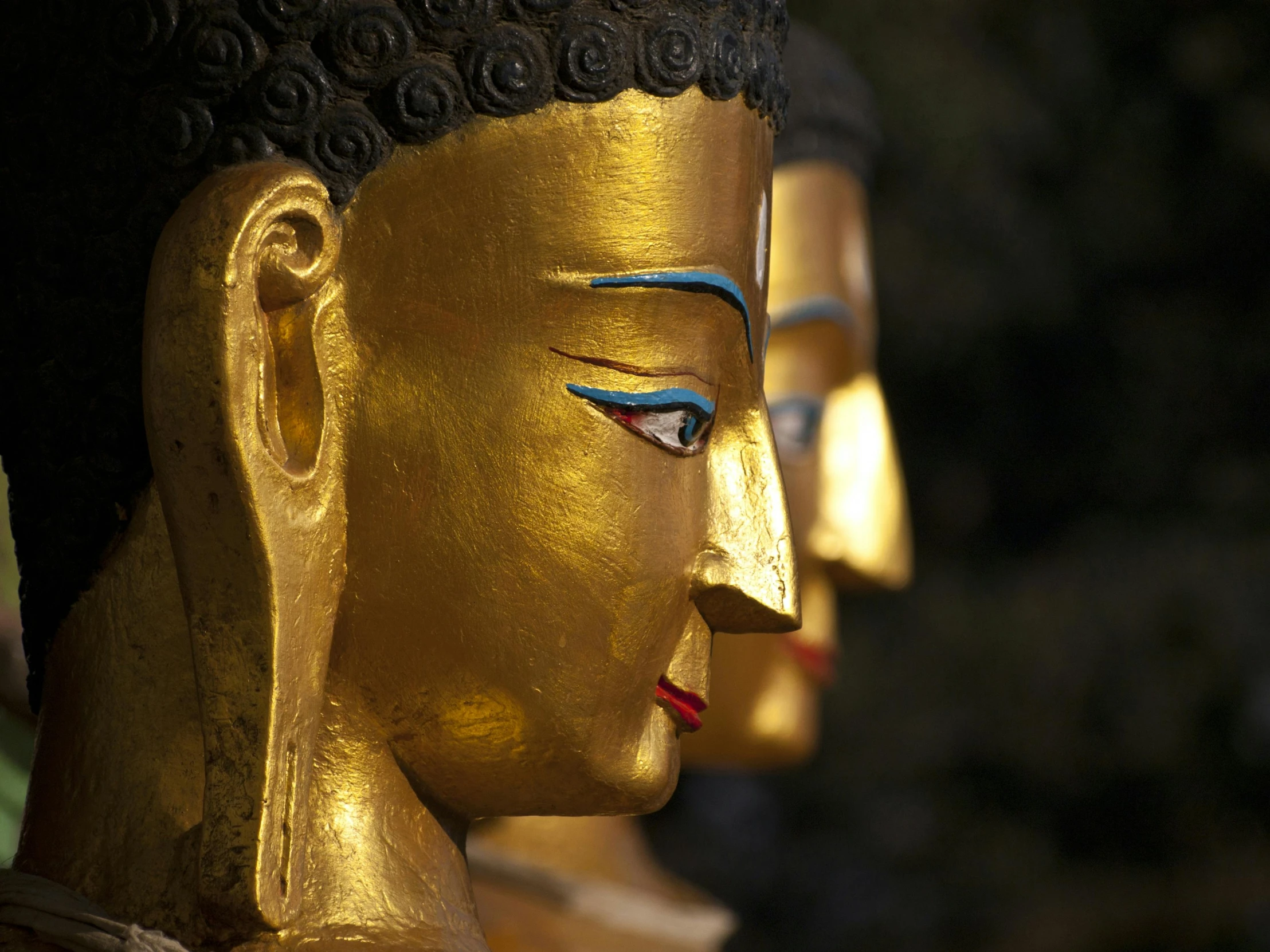 golden buddha statues sit against trees and light