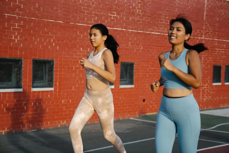 two women jogging on pavement in front of red brick building