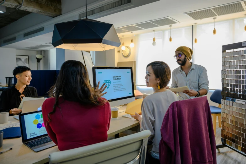 two men, one woman and man are standing in front of a computer screen