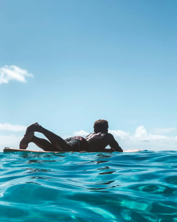 man laying in the ocean lying on a surfboard