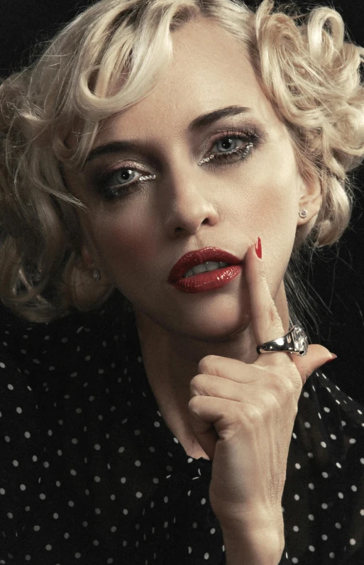 lady with red lipstick and a black dotted shirt holds a hand under her chin