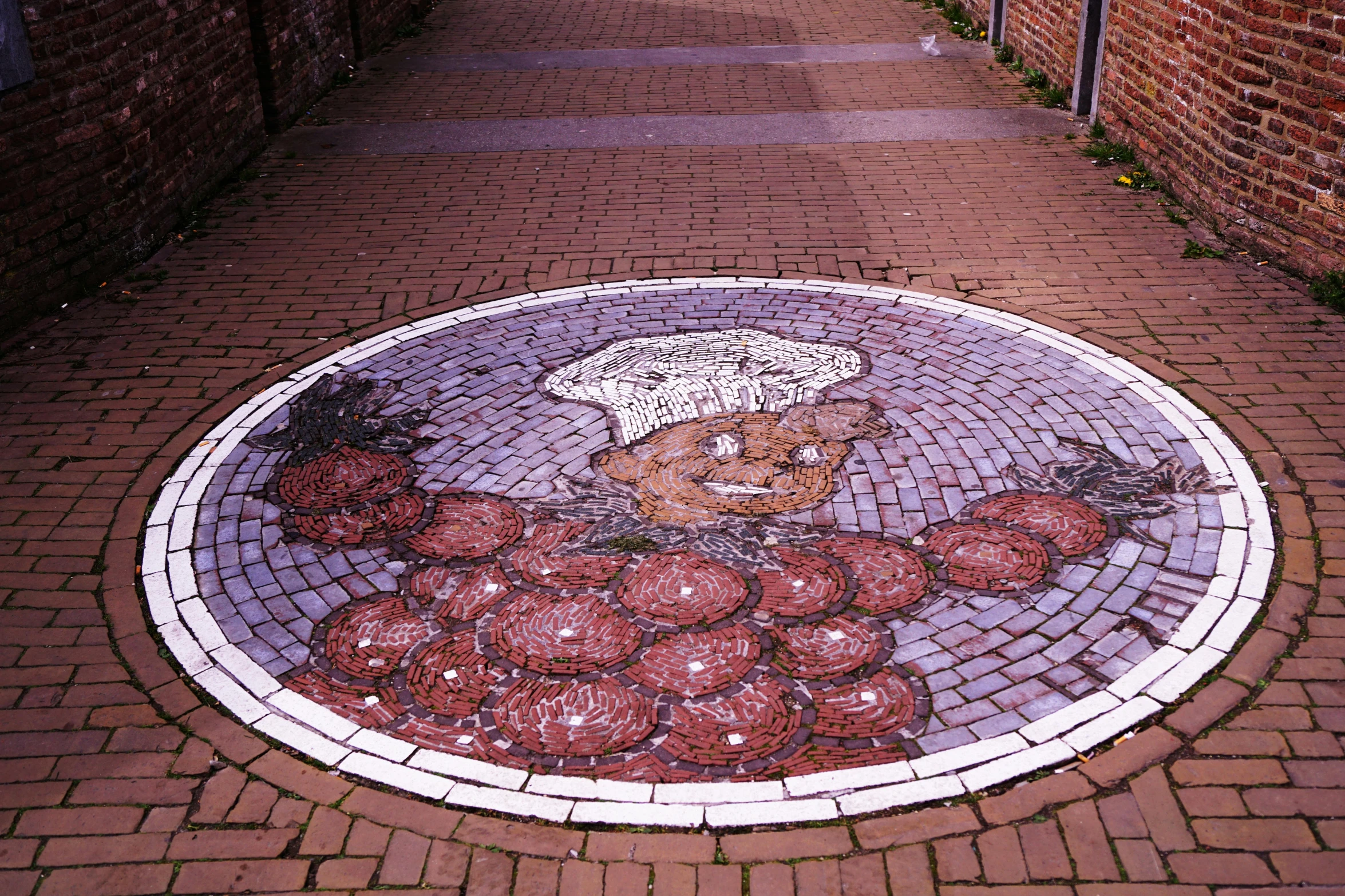 a tile mural depicting the head and hands of an ancient man on a circle of brick walkways