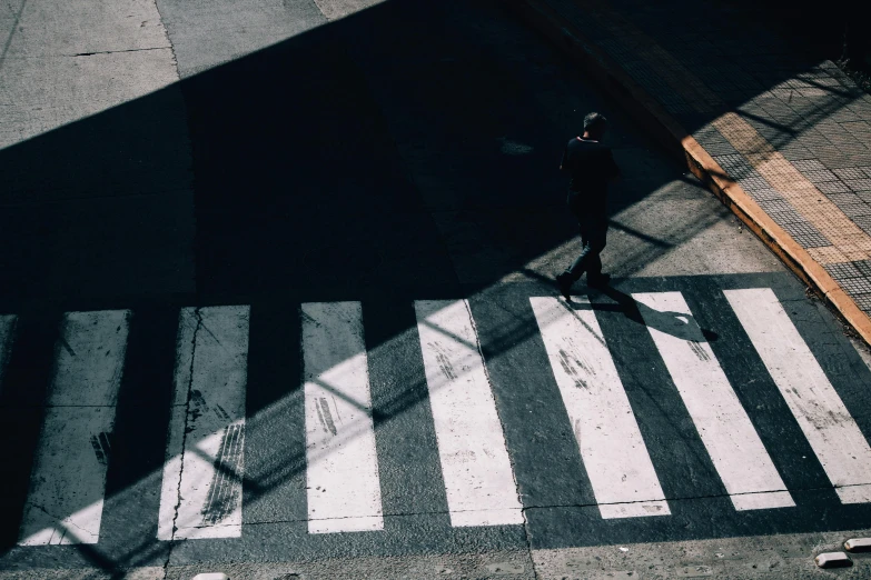 an overhead view shows the shadow of a man crossing an intersection