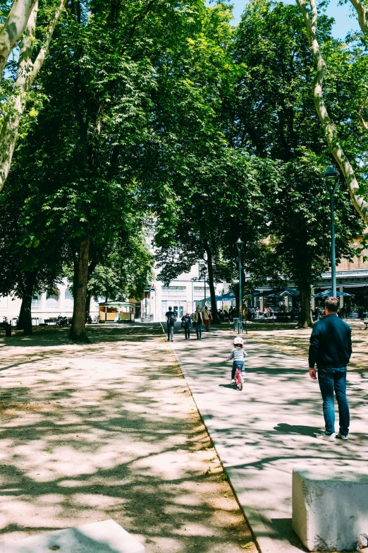 a man walking along a path between trees with children playing on the walkway