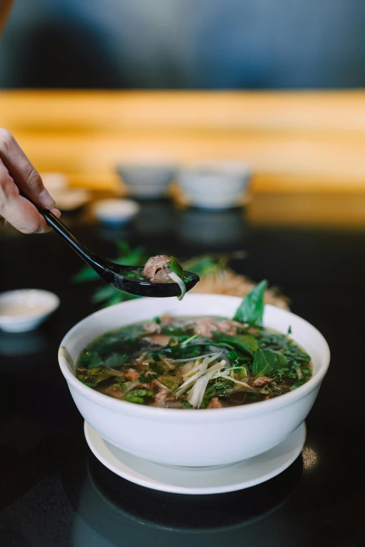 person holding spoon over bowl of soup with vegetables on it