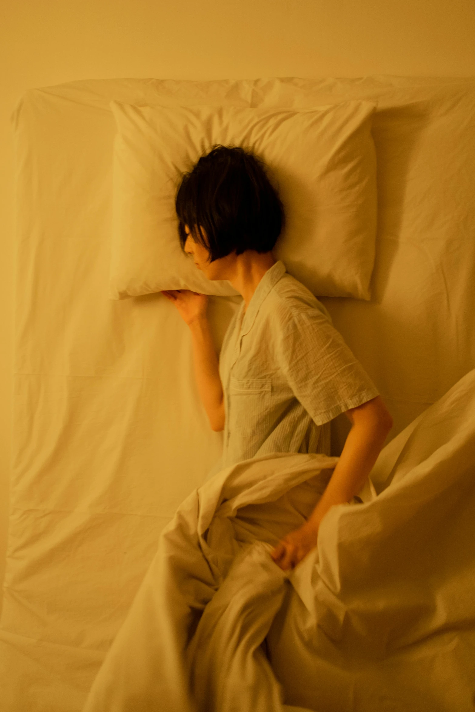 an asian boy with dark hair laying in a white bed