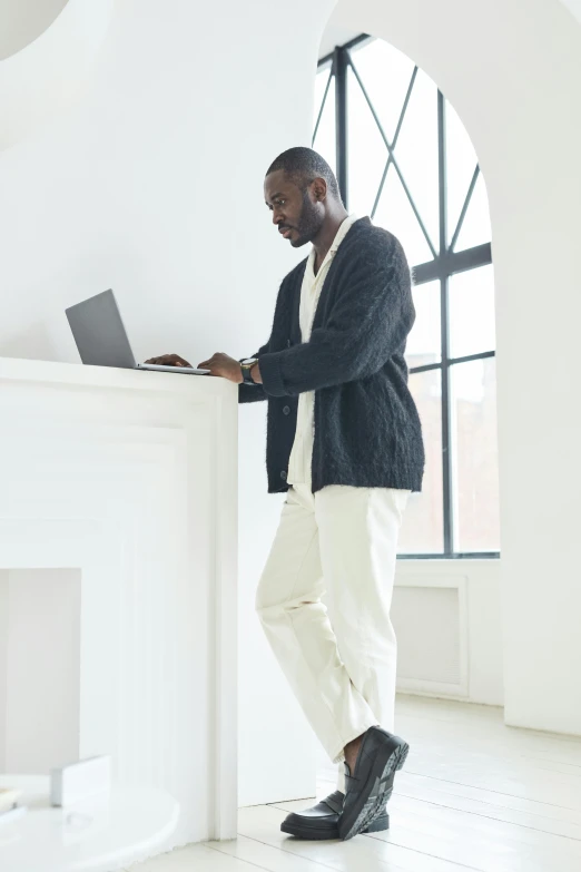 a black man is standing and looking at his laptop