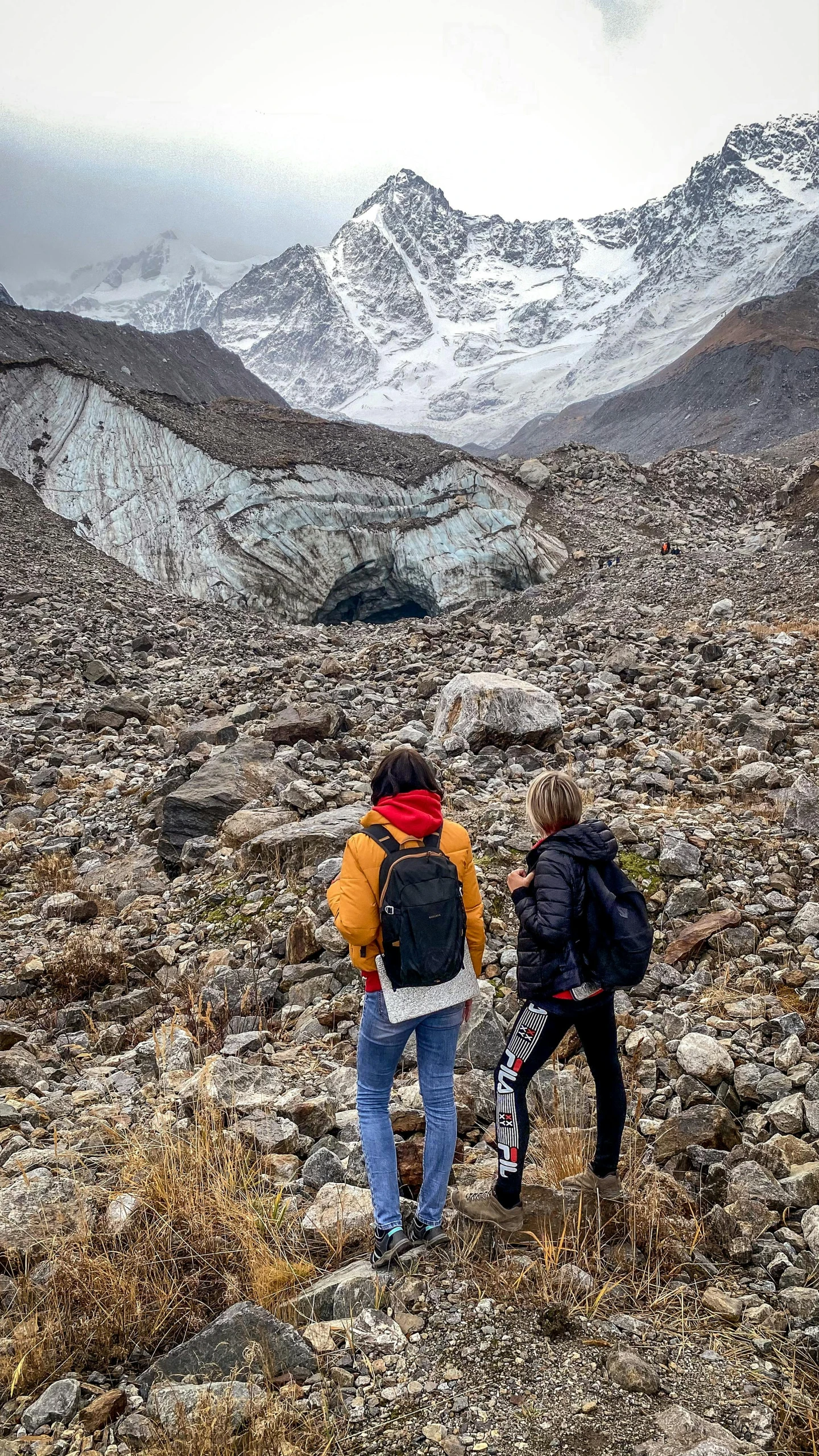 two people hiking in a field with some mountains behind them