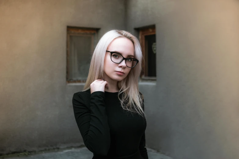 a blonde woman wearing glasses stands in an alley