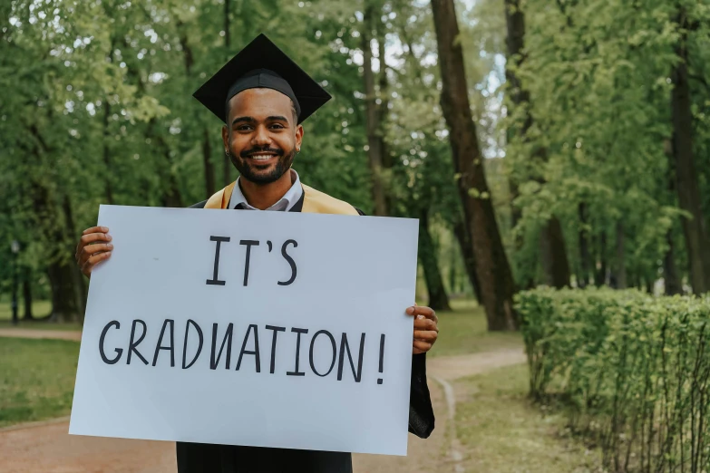 man with graduation hat and sign that says it's graduation
