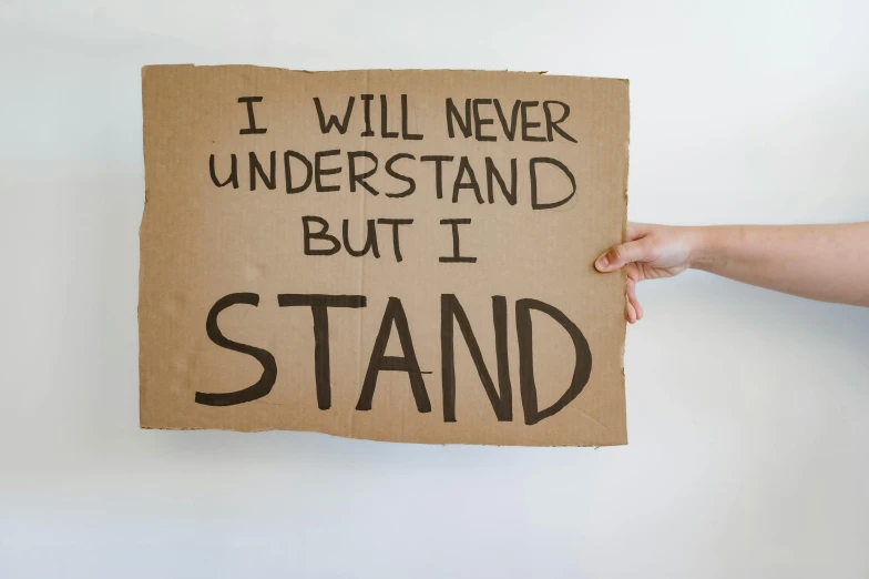 a cardboard sign with i will never understand but i stand