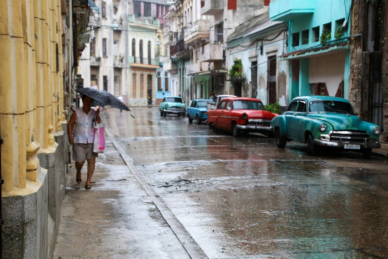 an old car is parked next to a woman holding an umbrella and walking in the rain