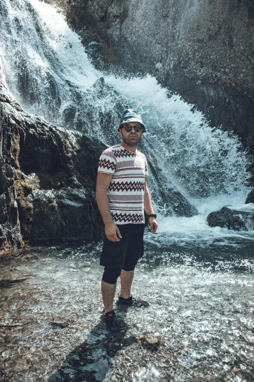 a man stands in a stream near waterfall