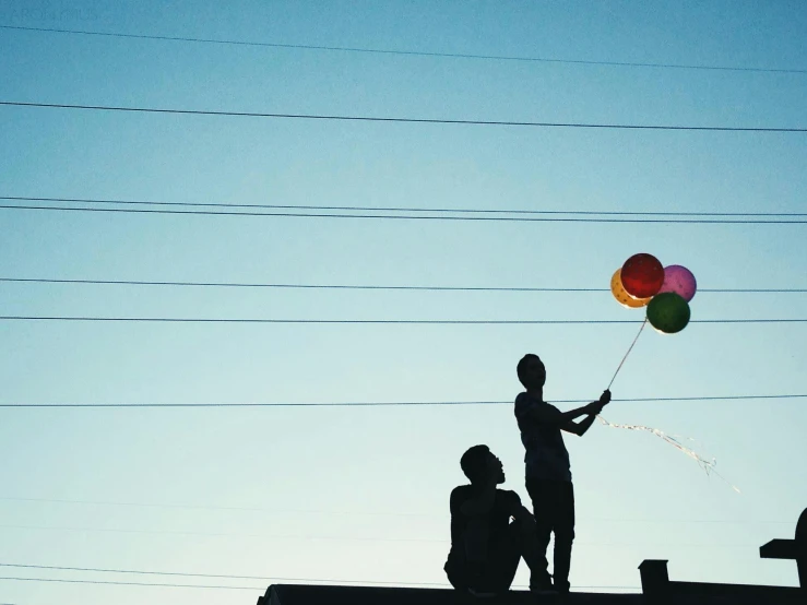 silhouette of two people with balloons and one is standing on a roof
