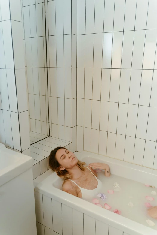 a woman sitting in a bathtub next to a tiled wall